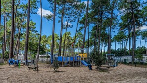 Een speeltuin met klimtoestellen en glijbanen, omgeven door hoge bomen en een heldere lucht.