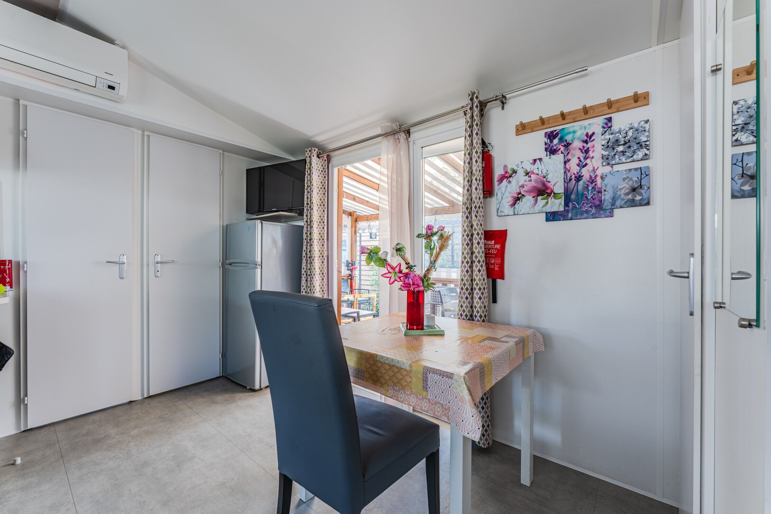 Eine kleine Küche mit Kühlschrank, einem Esstisch mit Stuhl und einem Fenster mit Vorhängen.