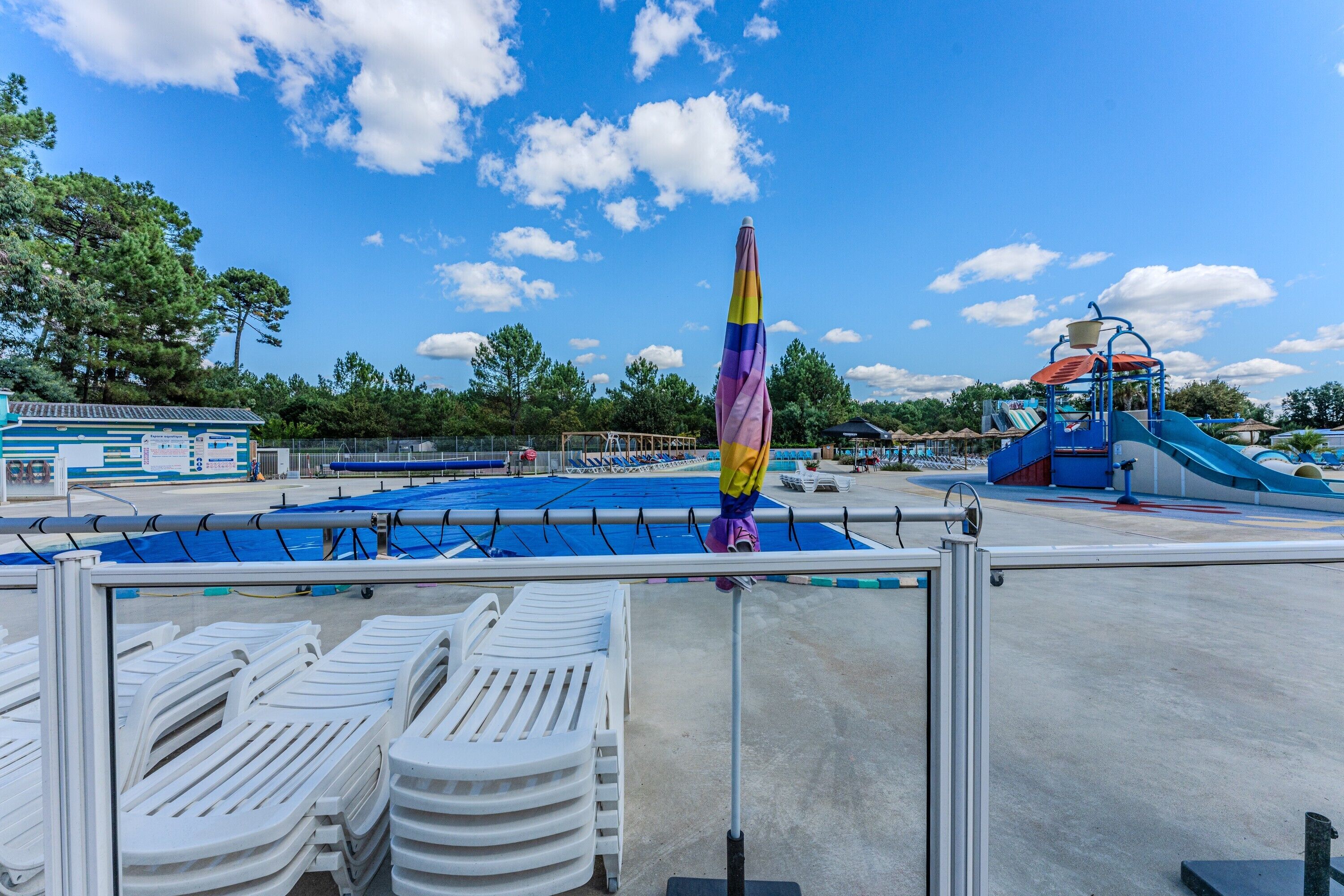Un espace piscine comprenant des chaises longues, un toboggan aquatique et un espace de repos abrité.