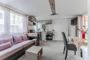 Un espacio habitable compacto con sofá, mesa de comedor, kitchenette y un refrigerador pequeño.