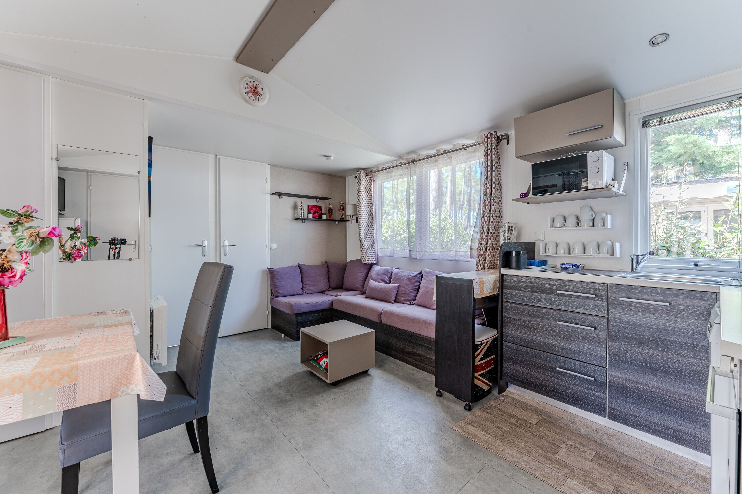 Un espace de vie compact comprenant un canapé, une table à manger, un coin cuisine et une fenêtre avec des rideaux.