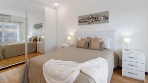 A modern bedroom with a large bed, a bedside table, a nightstand, a mirror, and a wall-mounted artwork. - Villa 'Alonzo' with Private Pool, Wi-Fi and Air Conditioning (Albufeira)