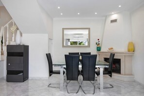 Un coin repas avec une table en verre, des chaises noires, une cheminée et un mur blanc orné d’un miroir.