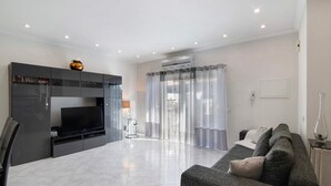 A modern living room with a flat-screen TV, a dark entertainment unit, a grey sofa, and a glass coffee table. - Villa 'Alonzo' with Private Pool, Wi-Fi and Air Conditioning (Albufeira)