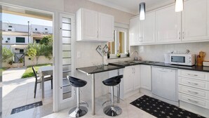 A modern kitchen with white cabinets, a black countertop, and two bar stools. - Villa 'Alonzo' with Private Pool, Wi-Fi and Air Conditioning (Albufeira)