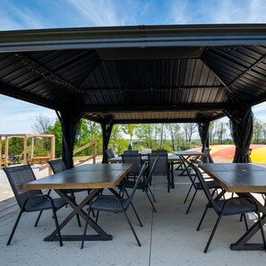 An outdoor covered patio with multiple tables and chairs, a wooden deck, and a view of the surrounding landscape. - 110) Loon Log Cabin. Close to Hocking Hills State Park and more! (Logan)