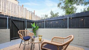 Een terras buiten met rieten meubels, een kleine tafel en een potplant.