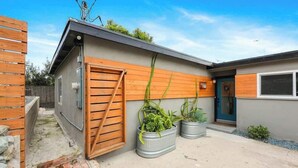 Een modern gelijkvloers huis met een houten deur, metalen plantenbakken en een klein betonnen terras.