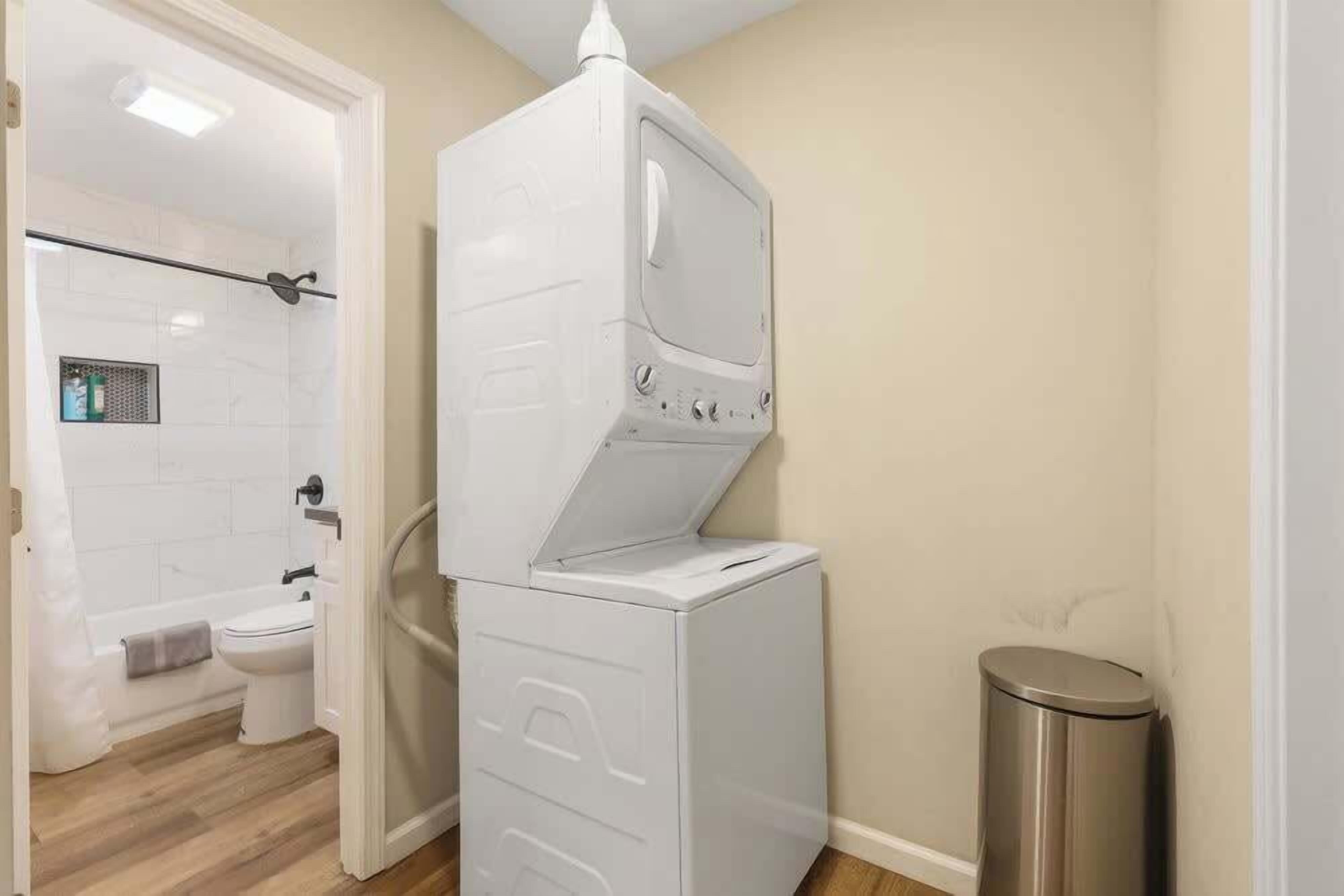 A compact bathroom with a white toilet, a shower area, and a stacked washer and dryer.