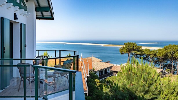 Un balcon donnant sur la mer, une terrasse en bois et un bâtiment aux volets verts.