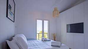 Une chambre moderne avec un lit, une grande fenêtre, un téléviseur et un luminaire suspendu.