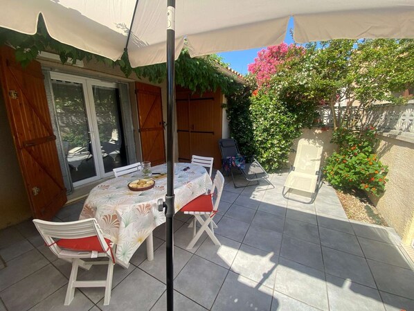 A patio with a table and chairs, a pergola, and a view of a garden with a fence.