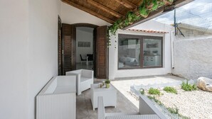 Une terrasse couverte, meublée de mobilier en osier, une clôture blanche et une vue sur la maison.