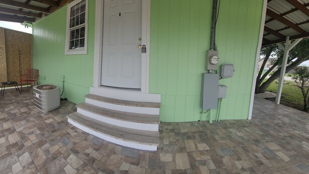 A green building with a white door, a set of steps leading to the entrance, and a covered porch area with chairs and a trash bin. - KASITA....5 min to river, 4min  to Christus S R hospital, state University 12min (San Marcos)