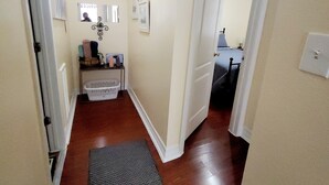 A narrow hallway with wooden flooring, a black mat at the entrance, and a door leading to a room with a bed and a desk. - KASITA....5 min to river, 4min  to Christus S R hospital, state University 12min (San Marcos)