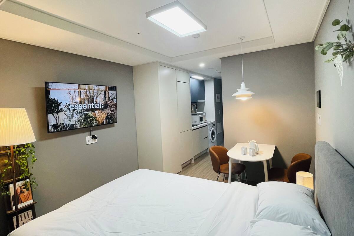Una habitación de hotel moderna con una cama, un escritorio con dos sillas, un televisor y una pequeña kitchenette.