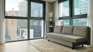 Una sala de estar moderna con un sofá, un jarrón decorativo y vistas a edificios de la ciudad a través de amplios ventanales.