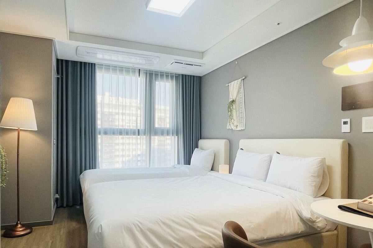 Una habitación de hotel con una cama grande, un escritorio, una silla, una lámpara y un ventanal con cortinas.
