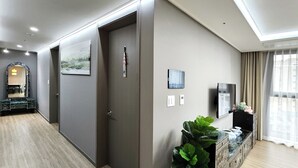 Una habitación de hotel moderna con piso de madera, un espejo grande, un cuadro, un televisor y una planta.