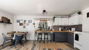Een kleine keuken met een eethoek, met een houten vloer, witte kastjes en een centraal kookeiland met krukken.