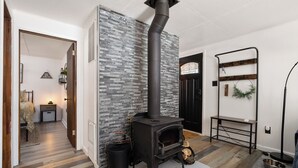 Een moderne woonkamer met een houtkachel, een stenen muur en een zwart metalen plank.