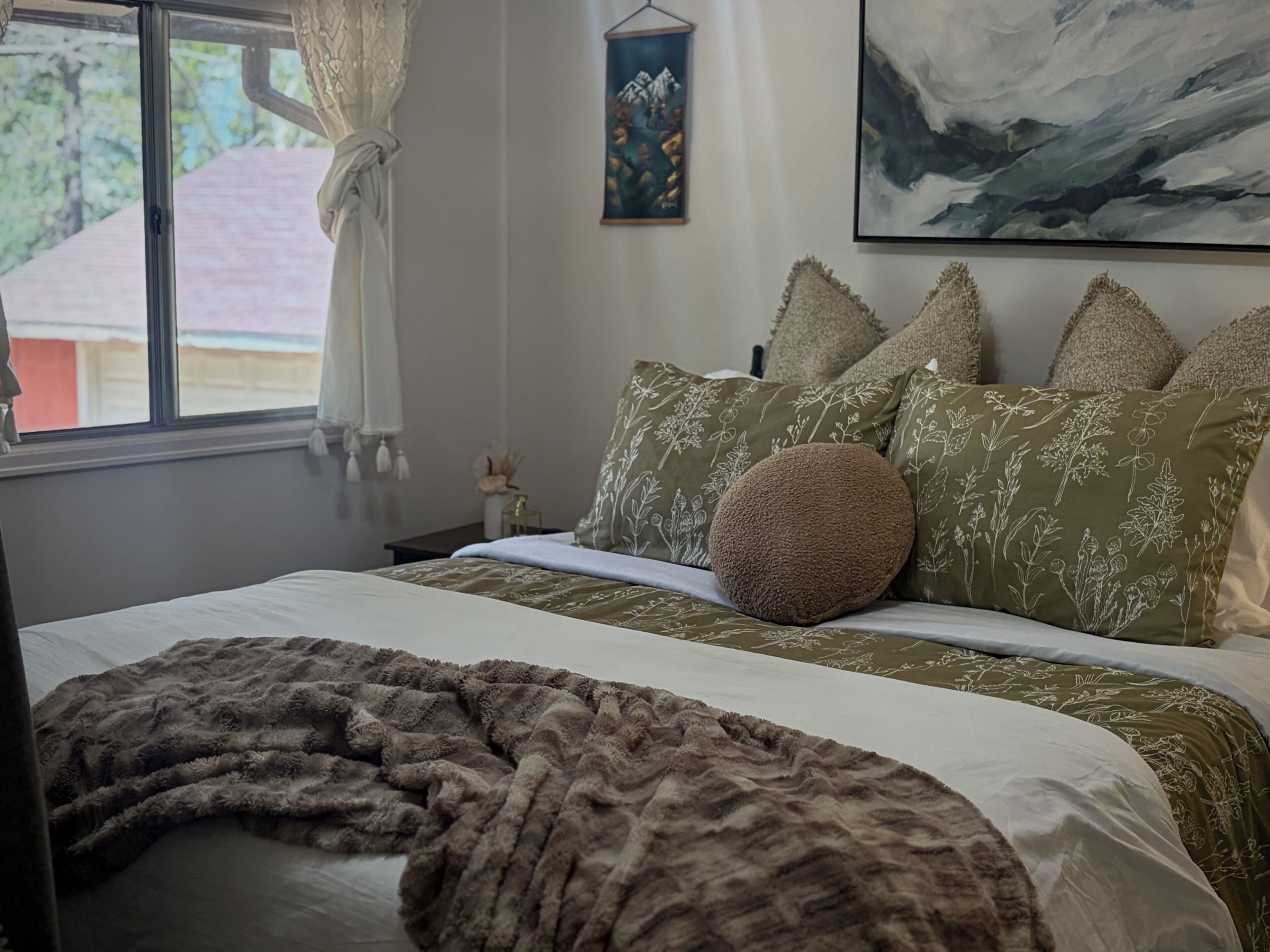 Una cama bien hecha con almohadas estampadas, un edredón mullido y un cuadro en la pared.
