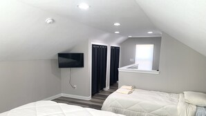 A bedroom with two beds, a TV mounted on the wall, a window with curtains, and a mirror.
