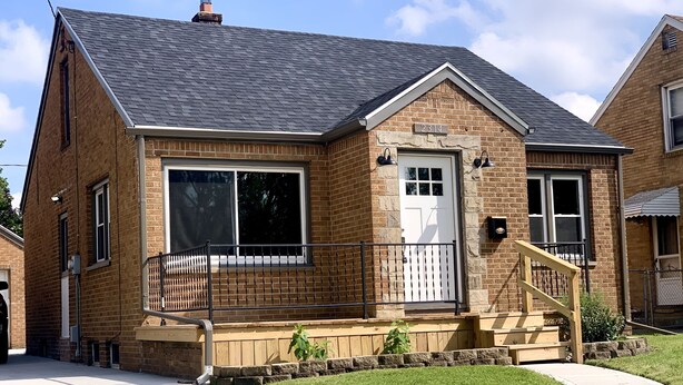 A two-story brick house with a white front door, large windows, and a small porch with a railing.