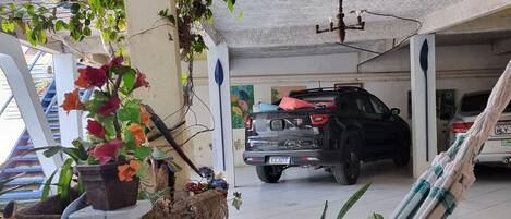 Área externa coberta com rede, plantas em vasos e um SUV estacionado.