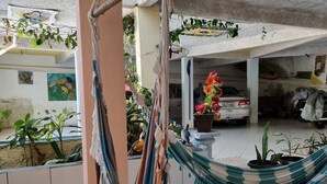 Una hamaca colgada en un porche, un coche estacionado y macetas con plantas.