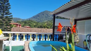 Zona de piscina con plantas en macetas, un suelo de baldosas y vistas a una montaña.