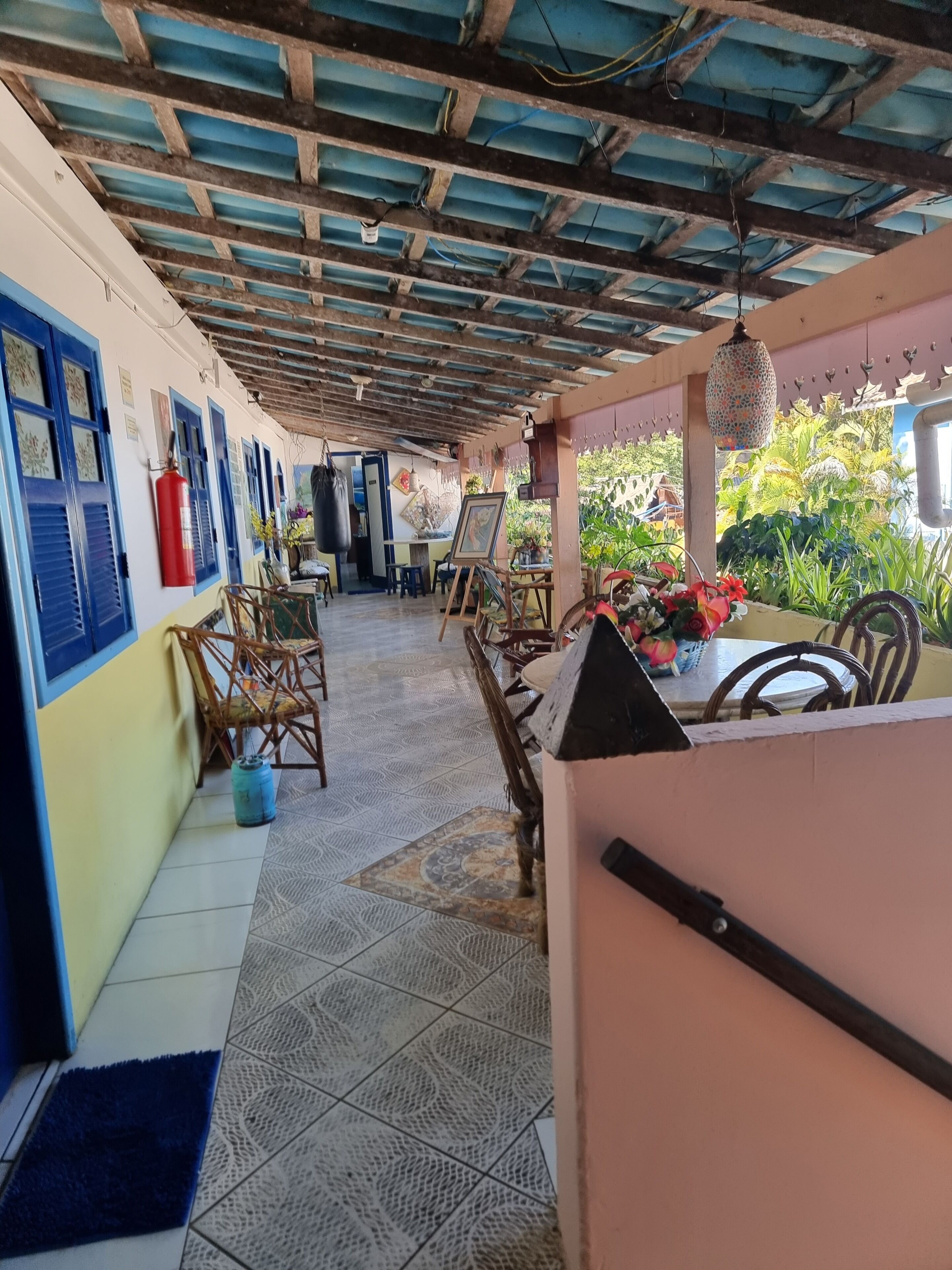 Un espacio al aire libre techado con suelo de baldosas, muebles de madera y un extintor en la pared.