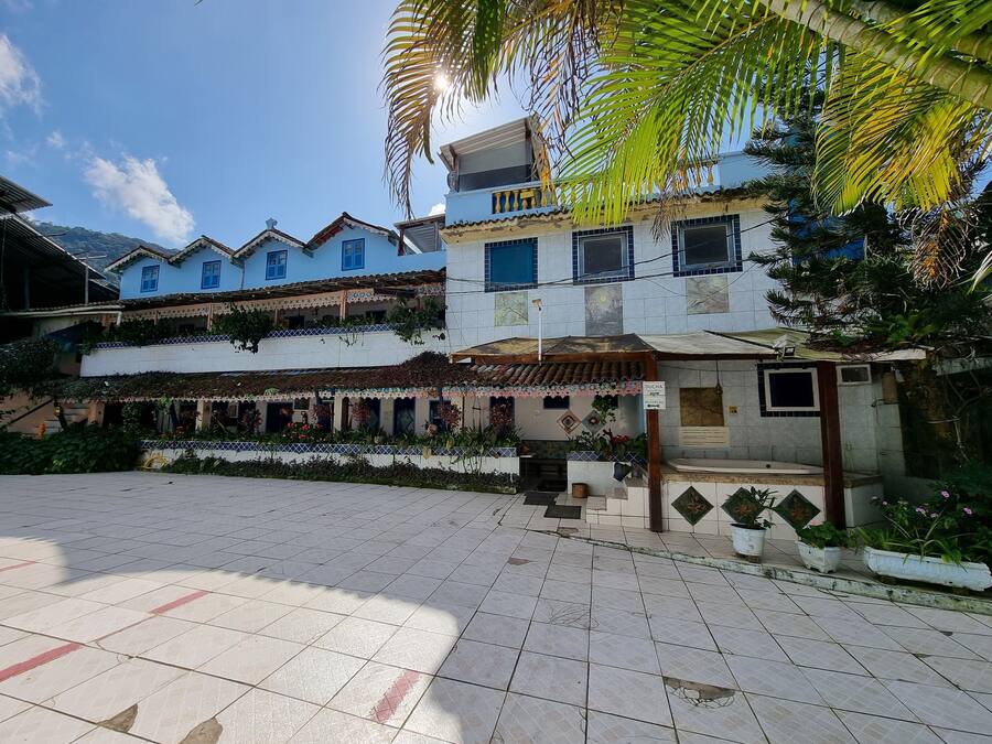 Um edifício com vários andares, fachada em azulejos, área de entrada coberta e um pátio com plantas em vasos.