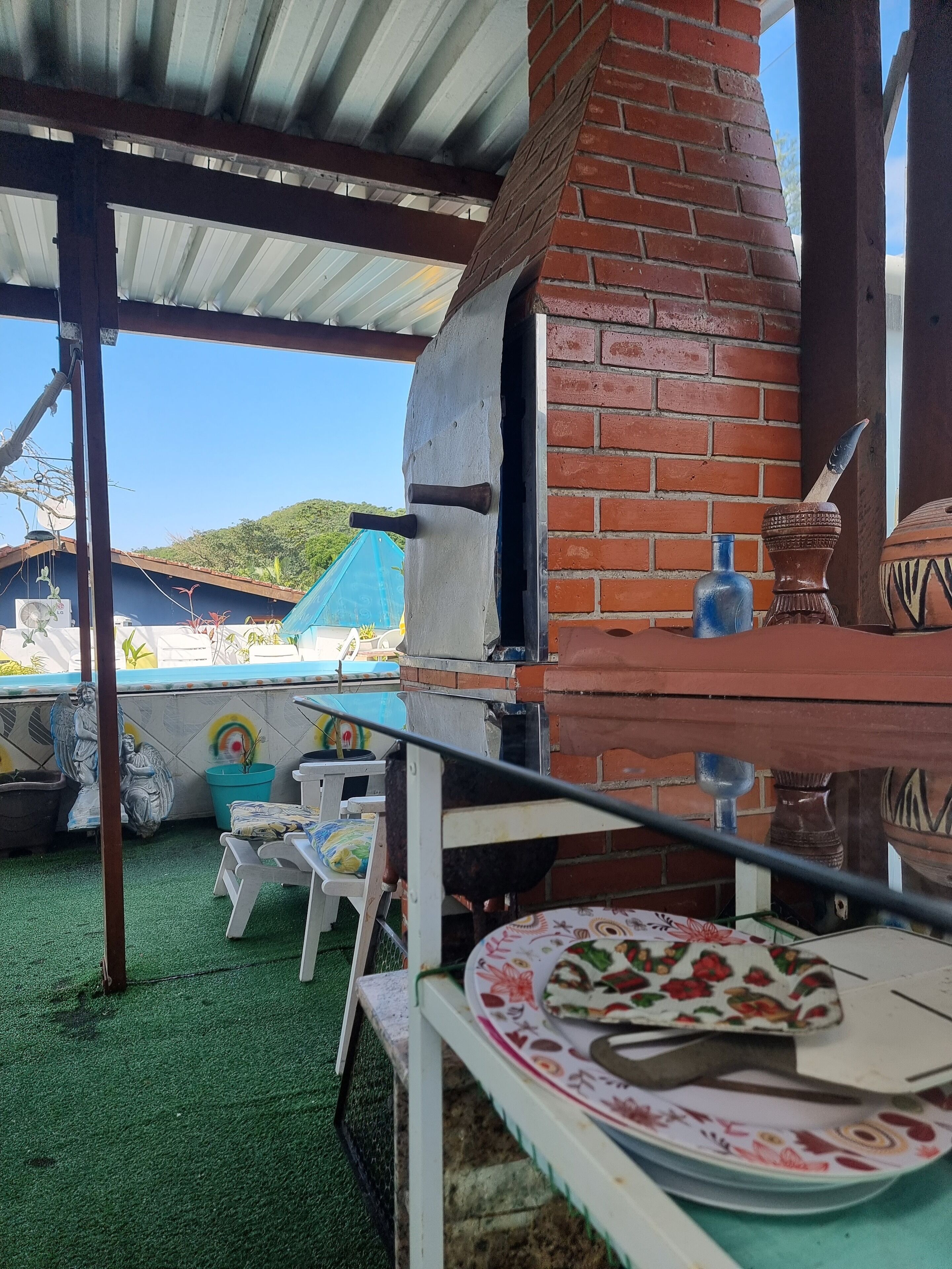 An outdoor patio area with a brick oven, a table with a plate and utensils, and a blue vase.