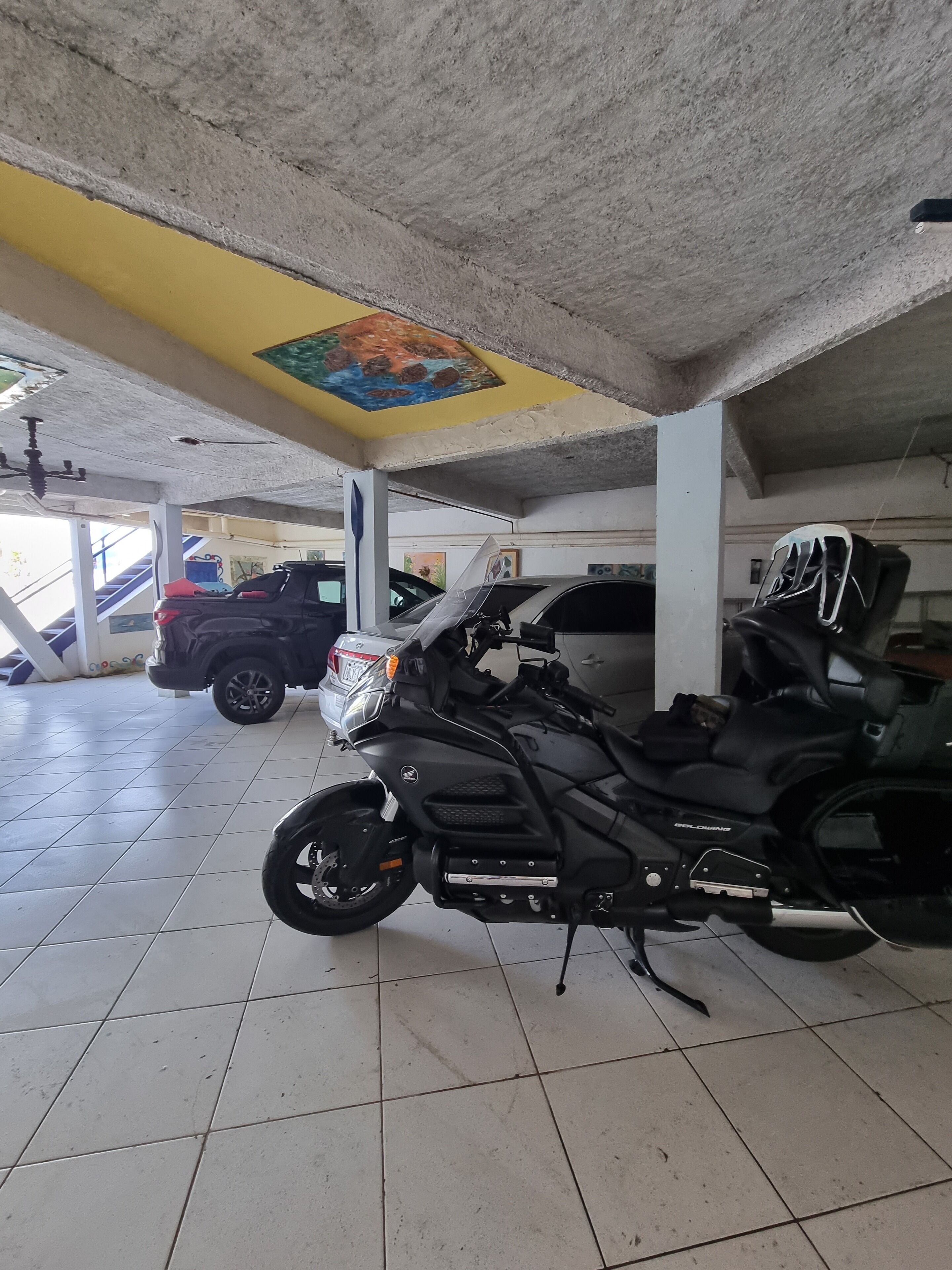 Una motocicleta estacionada en un área de estacionamiento techada, con piso de baldosas y techo amarillo.