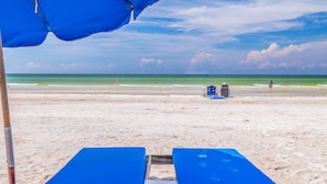 Une plage avec un parasol bleu, une chaise longue et une chaise de plage.
