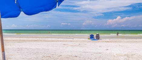 Una playa con una sombrilla azul, una tumbona y una silla de playa.