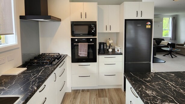 Una cocina moderna con armarios blancos, una estufa negra, un microondas y un refrigerador.