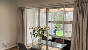 Un comedor moderno con una mesa de vidrio, dos sillas y un jarrón con flores blancas.