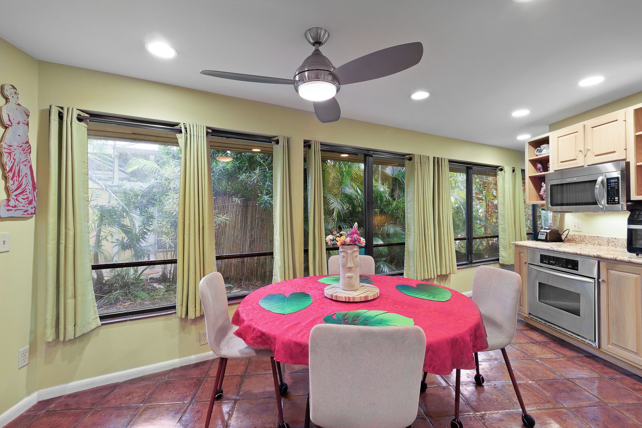A dining area with a round table, chairs, a ceiling fan, and a kitchen with a microwave and oven.