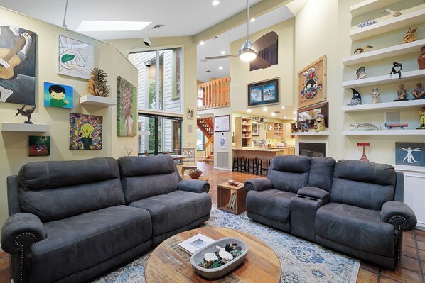 A spacious living room with two dark leather sofas, a wooden coffee table, and various artworks on the walls.