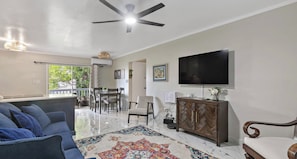 A living room with a ceiling fan, a flat-screen TV, a sofa, a coffee table, and a patterned rug.