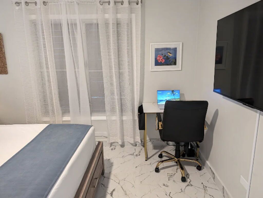 Une chambre à coucher avec un lit, un bureau avec un ordinateur, une chaise et une fenêtre avec des rideaux.