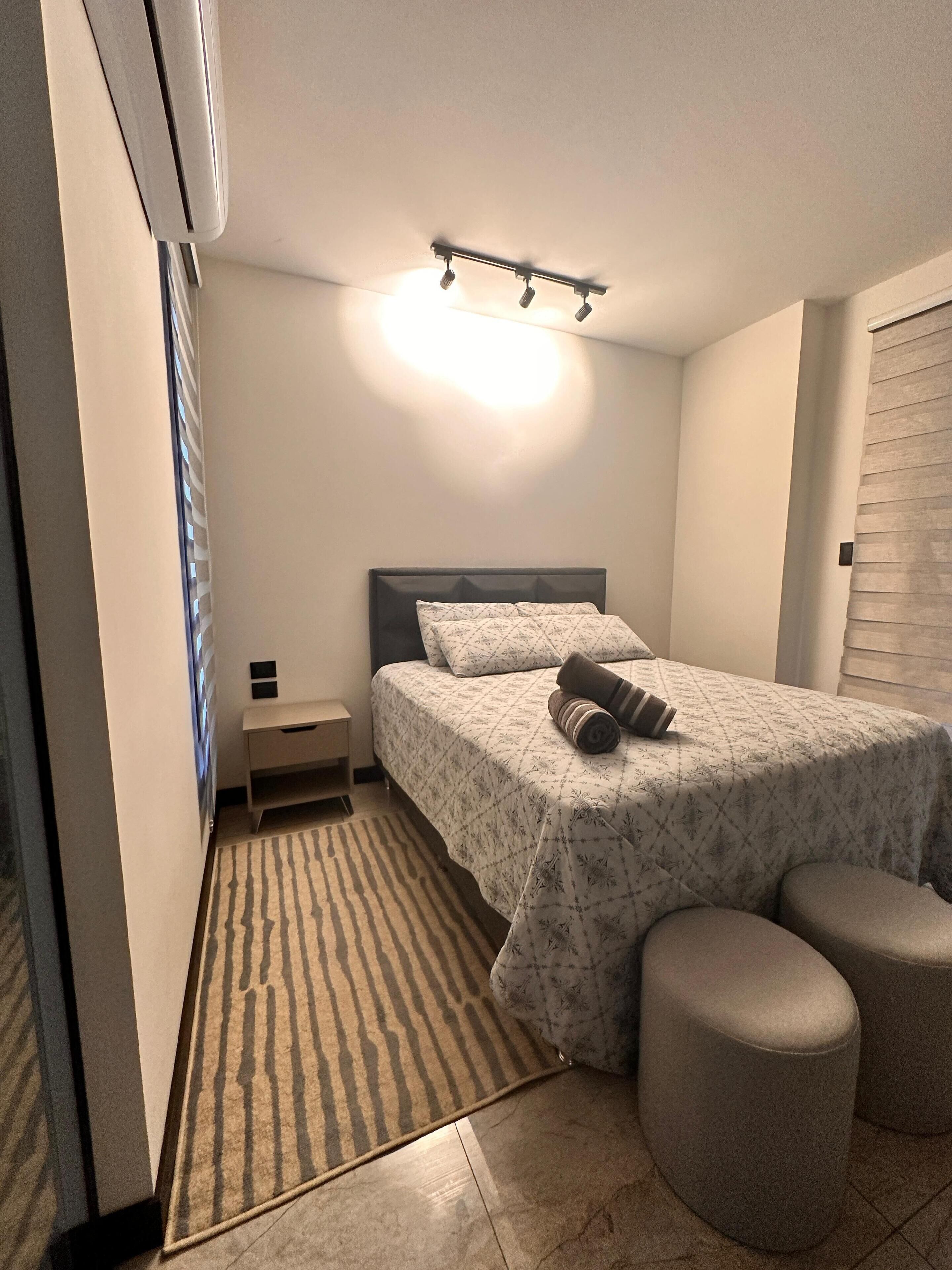 A bedroom with a bed, bedside table, and a small stool.