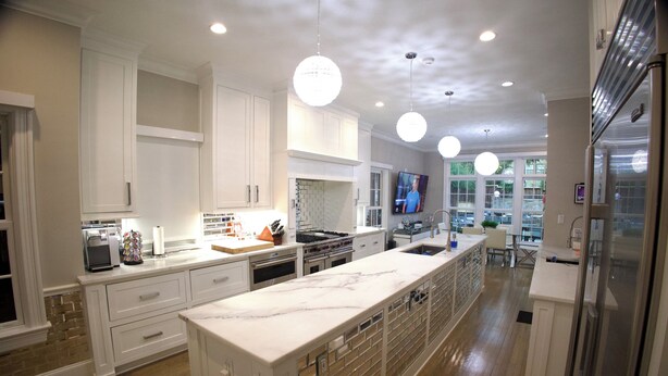 Una cocina moderna con armarios blancos, una isla de mármol e iluminación colgante.
