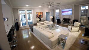 Una sala de estar amplia con un sofá modular grande, una mesa de centro de vidrio y un televisor de pantalla plana montado en la pared.