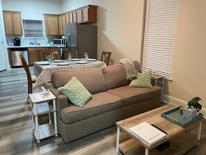 Una sala de estar con un sofá marrón, una mesa de centro, una mesita auxiliar y una zona de comedor con una mesa preparada para cuatro.