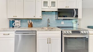 A kitchen with white cabinets, a blue tiled backsplash, a coffee maker, a microwave, a dishwasher, and an oven. - Renovated 2bed / 1bath North End of Anna Maria, 2min walk to the beach  (Anna Maria)