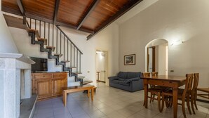 Amplia sala de estar con una escalera de madera, un sofá, una mesa de comedor con sillas y una chimenea.
