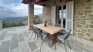 A stone building with a wooden table and chairs on a balcony.